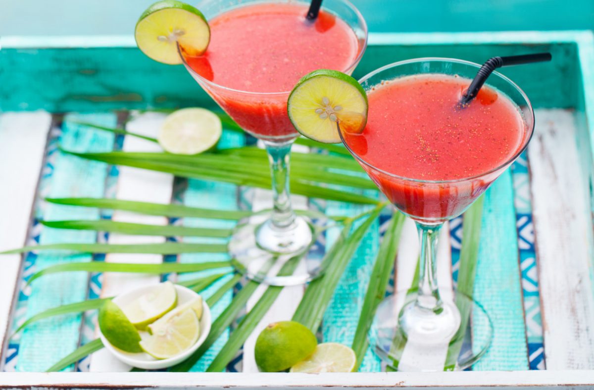 Strawberry margarita cocktail on colorful wooden background with palm leaf